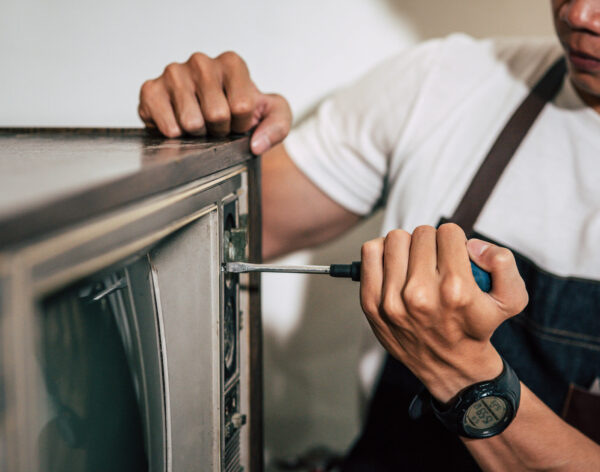 The mechanic uses a screwdriver to tighten the screws on the TV. Selective focus.