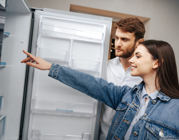 Young couple selecting new refrigerator in household appliance store, close up